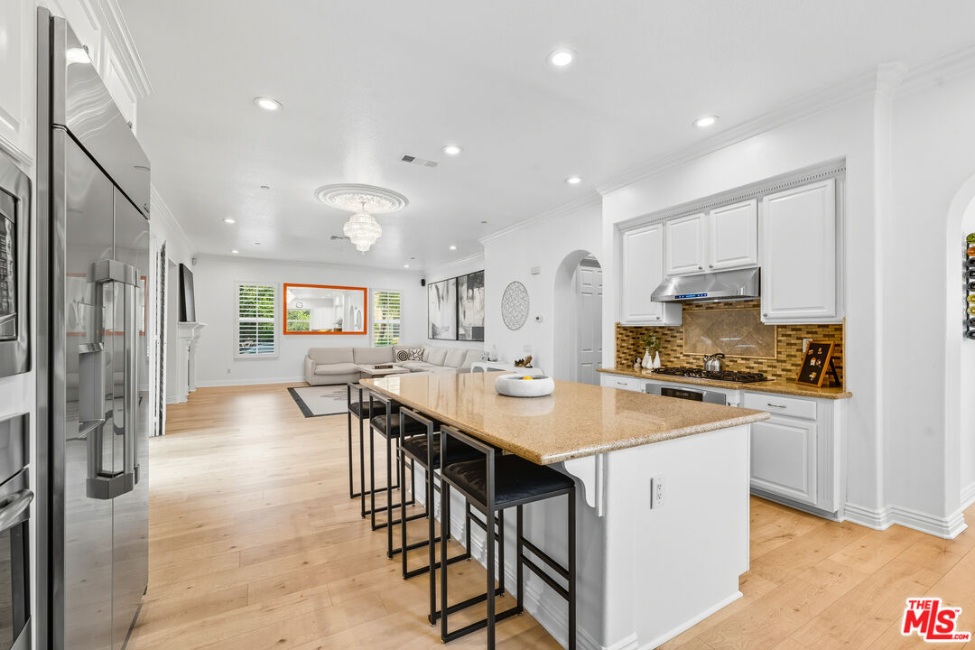 22074 Sagebrook Road Chatsworth, CA 91311 - Photo 8 of 35 a kitchen with stainless steel appliances granite countertop a stove top oven a refrigerator a sink and a dining table with wooden floor
