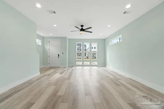 an empty room with chandelier fan and windows