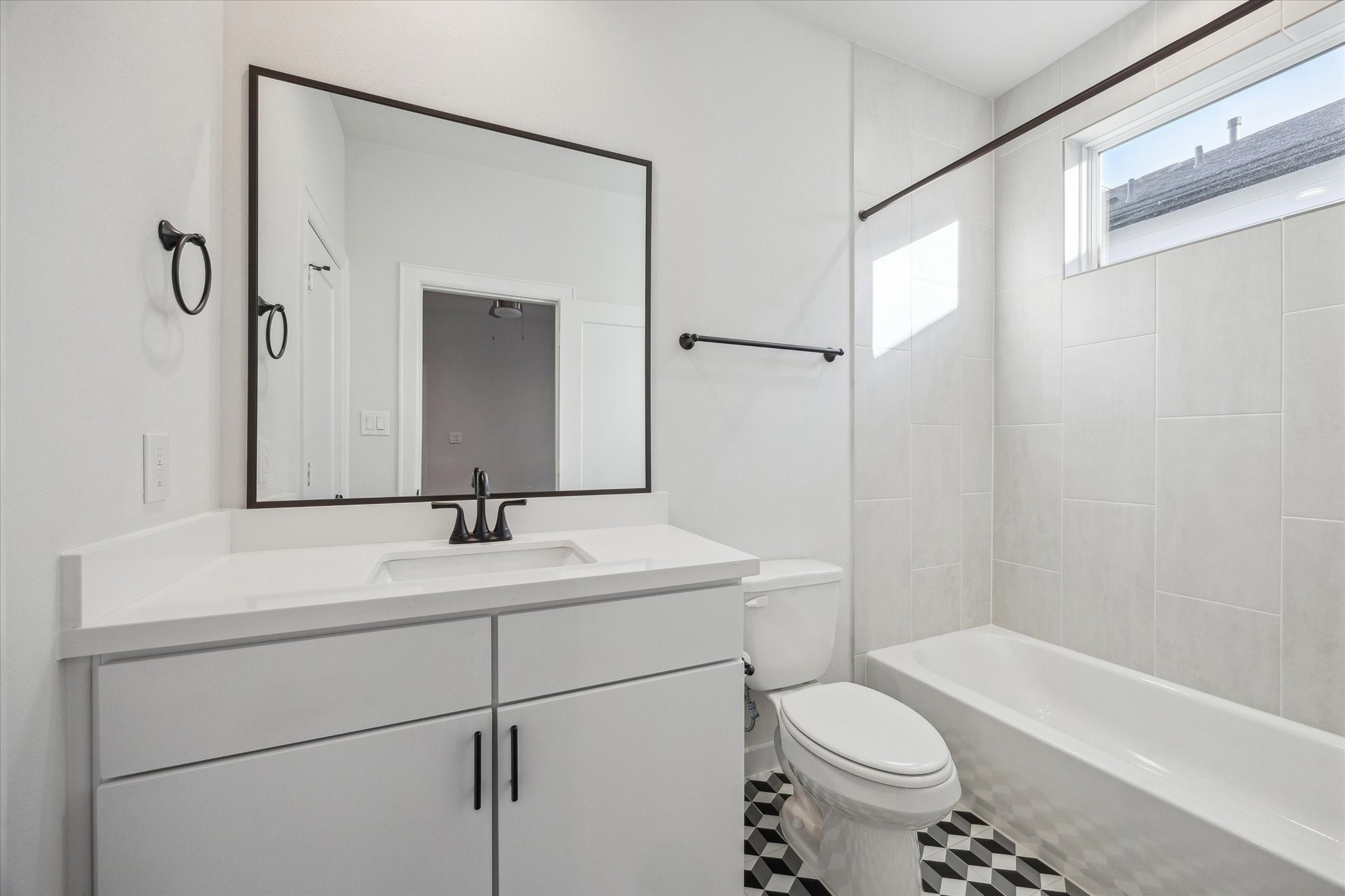 1603 Patterson Street, Unit E Houston, TX 77007 - Photo 24 of 32 This bathroom features a modern design with a large mirror, sleek vanity, and black fixtures. It has a bathtub, tiled walls, and a window for natural light, complemented by geometric patterned floor tiles for a stylish touch.