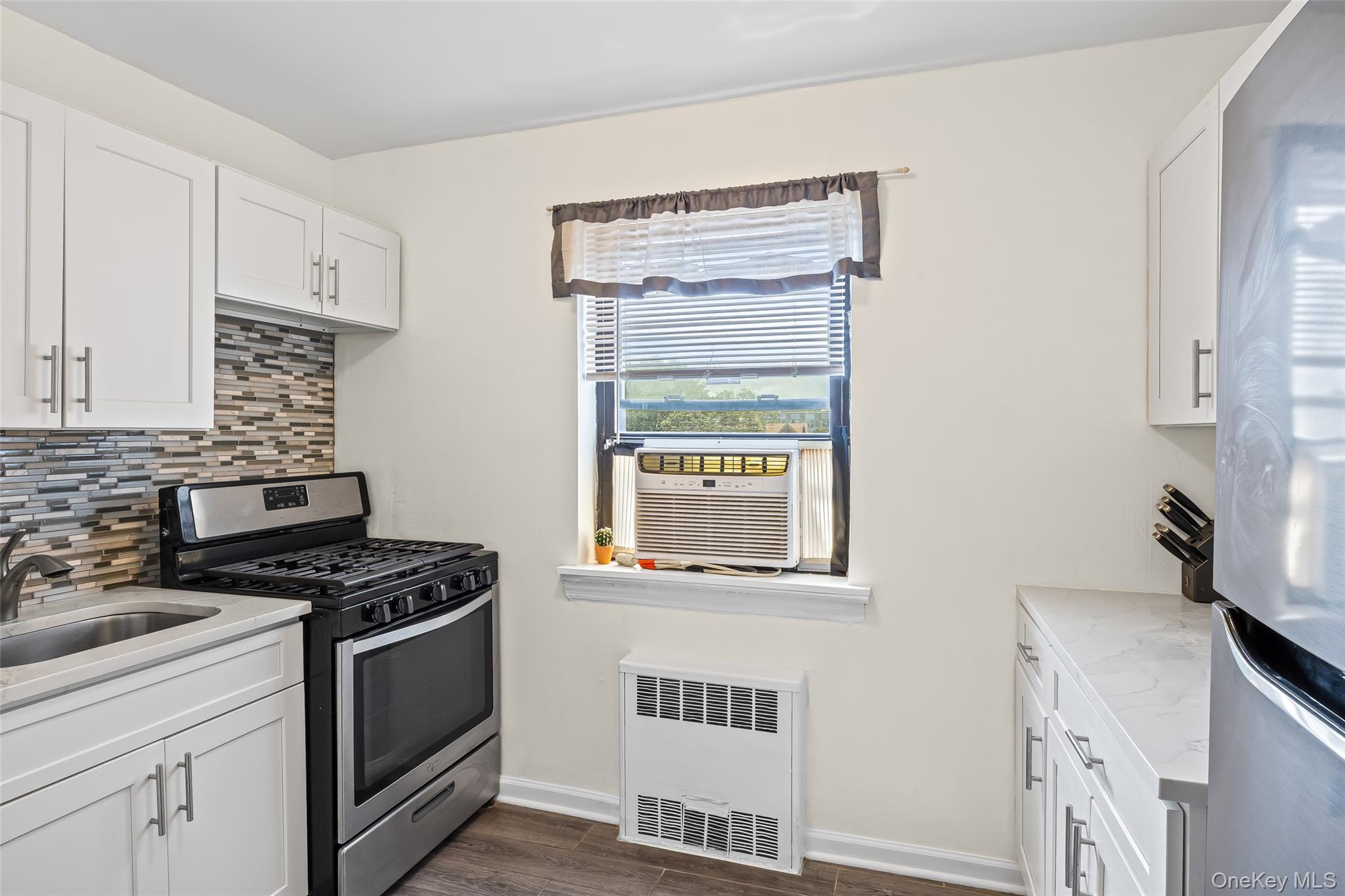 147-10 84th Road, Unit 4G Queens, NY 11435 - Photo 3 of 13 Kitchen featuring appliances with stainless steel finishes, tasteful backsplash, radiator, dark wood-type flooring, and white cabinets