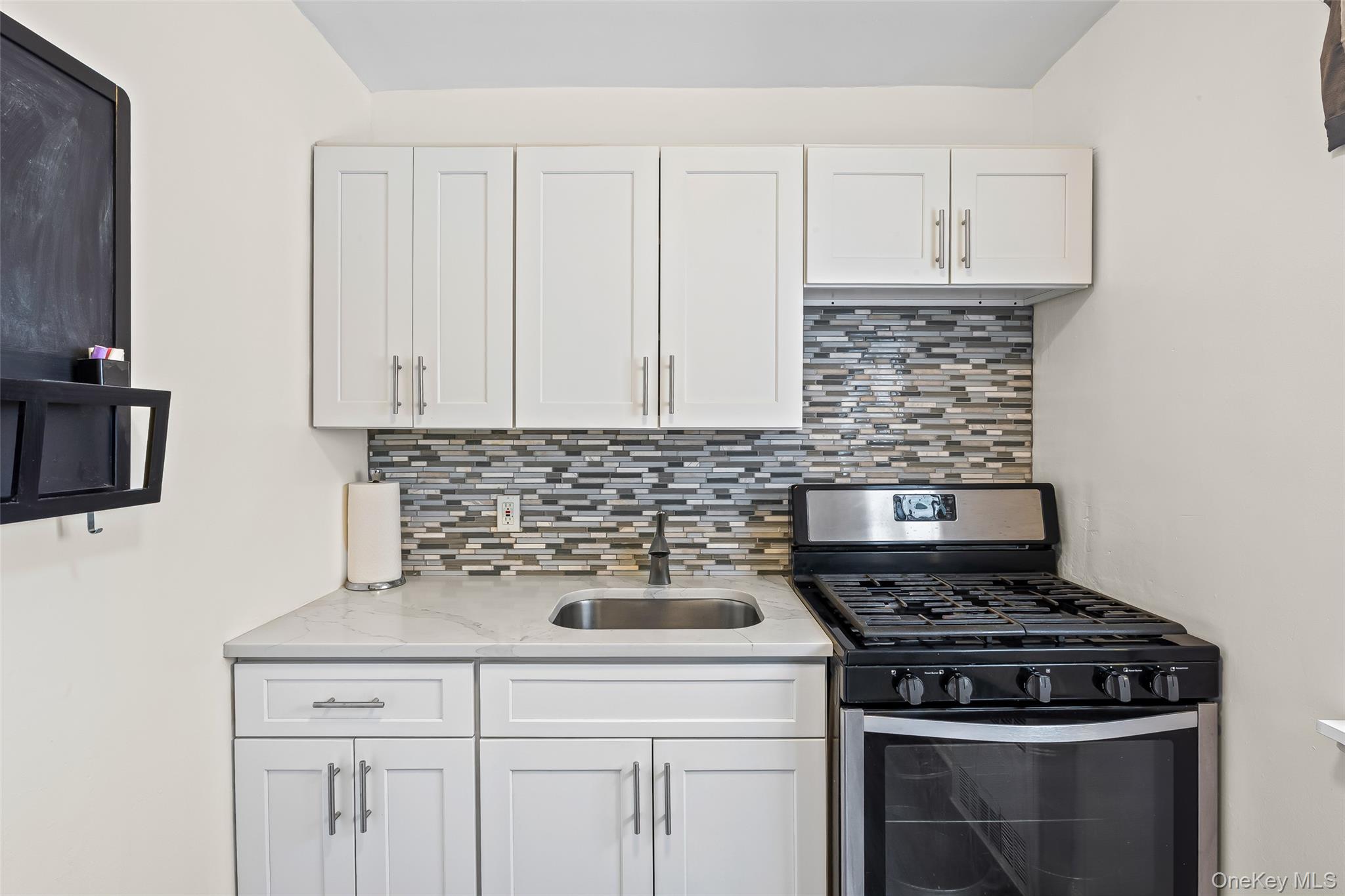 147-10 84th Road, Unit 4G Queens, NY 11435 - Photo 4 of 13 Kitchen with tasteful backsplash, gas stove, white cabinetry, and light stone countertops