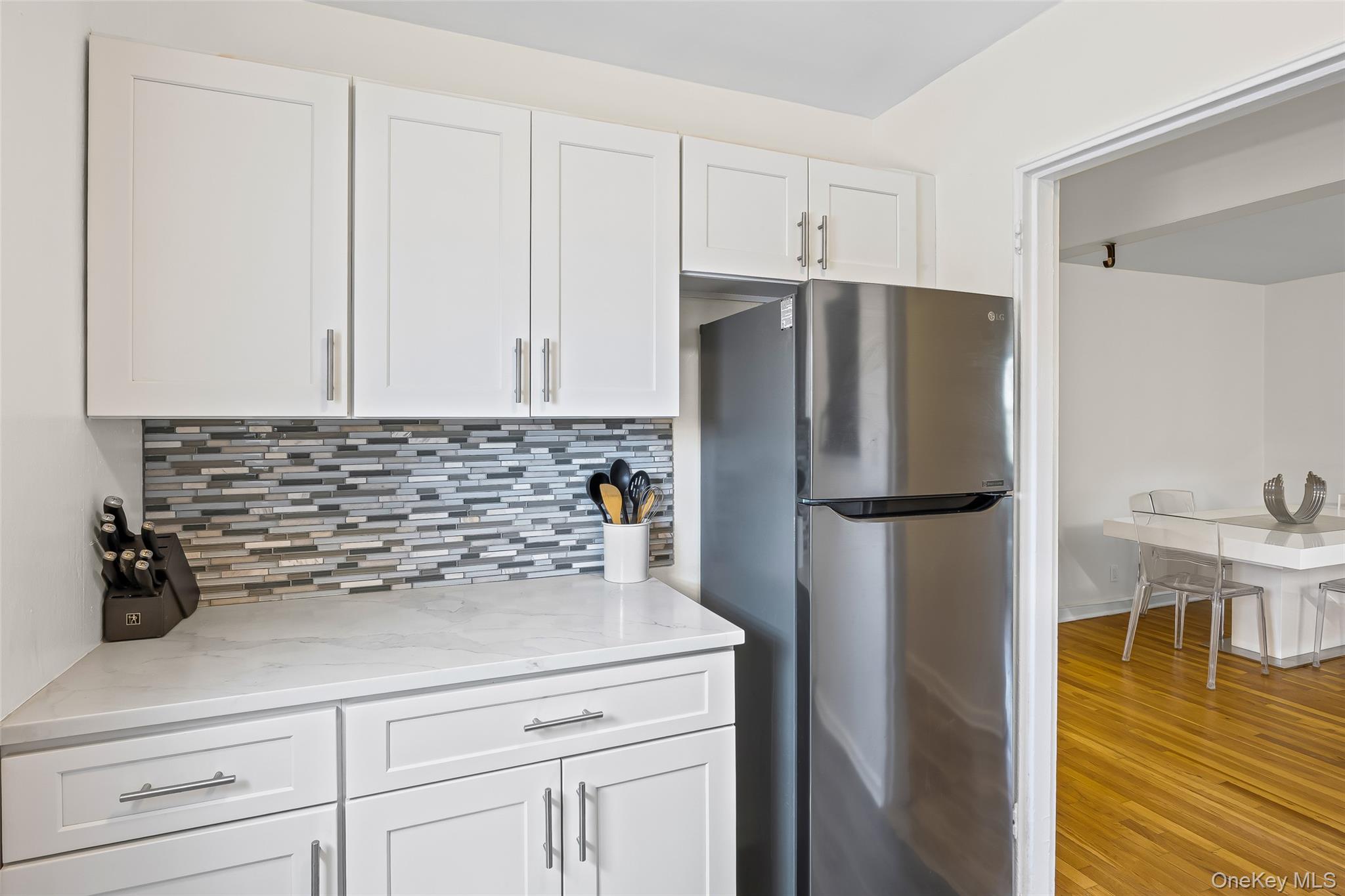 147-10 84th Road, Unit 4G Queens, NY 11435 - Photo 5 of 13 Kitchen with freestanding refrigerator, backsplash, white cabinetry, light stone counters, and light wood-style flooring