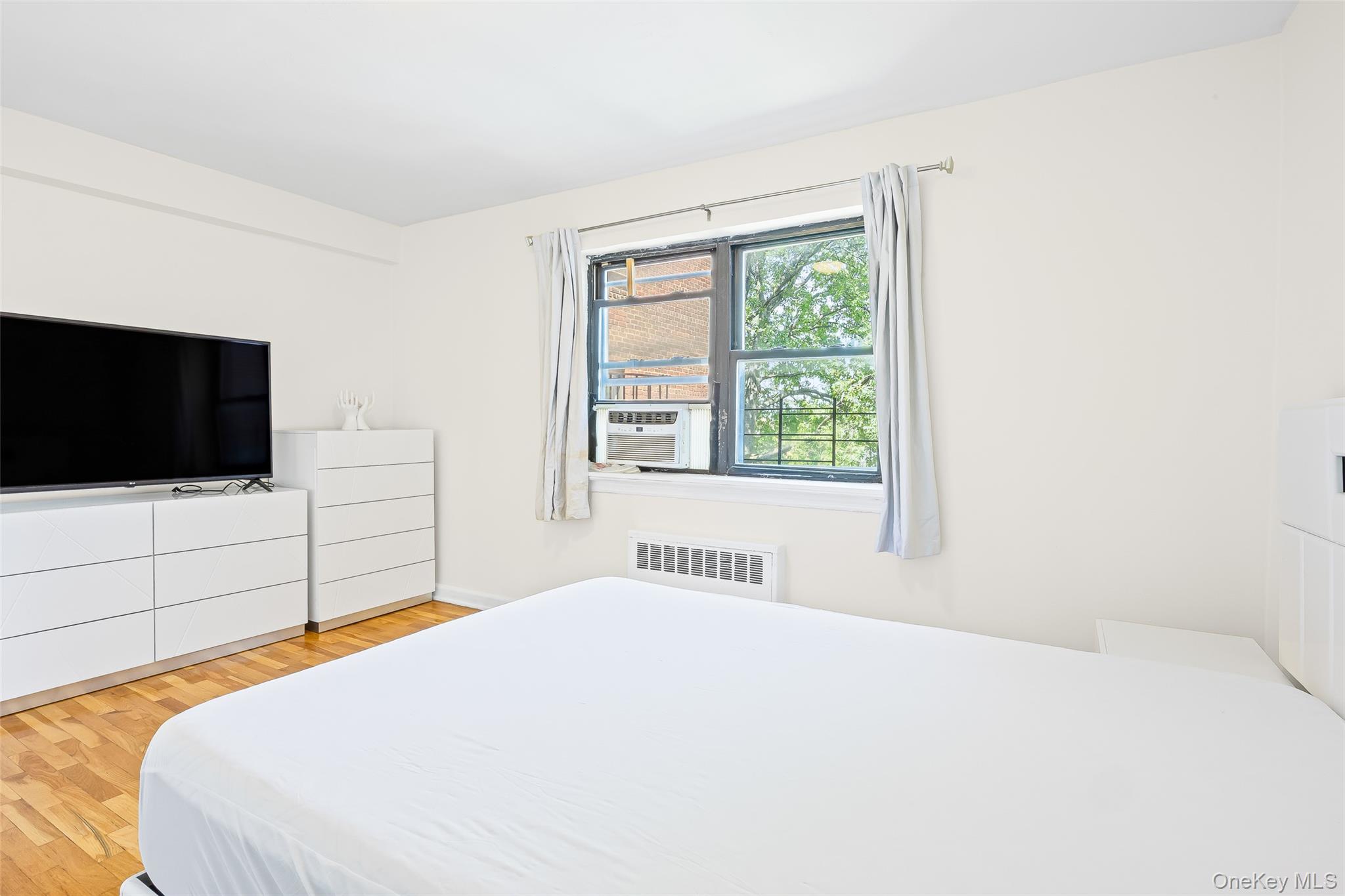 147-10 84th Road, Unit 4G Queens, NY 11435 - Photo 8 of 13 Bedroom featuring light wood-style flooring, radiator heating unit, and cooling unit