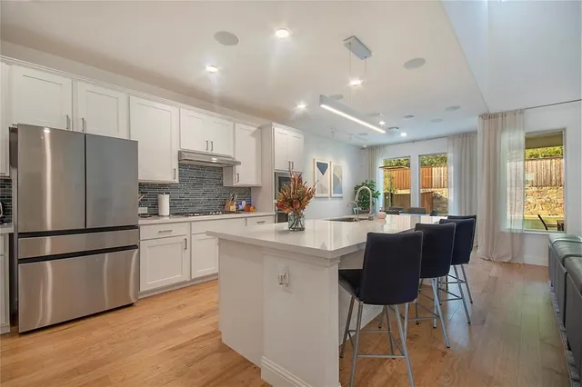 a kitchen with stainless steel appliances granite countertop a refrigerator a stove a sink a dining table and chairs with wooden floor