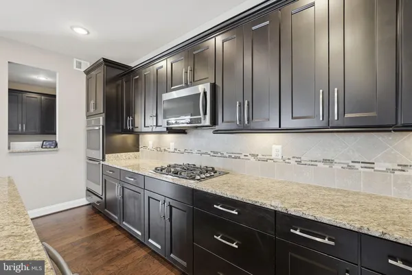 a kitchen with stainless steel appliances granite countertop a stove top oven a sink dishwasher a dining table and chairs with wooden floor