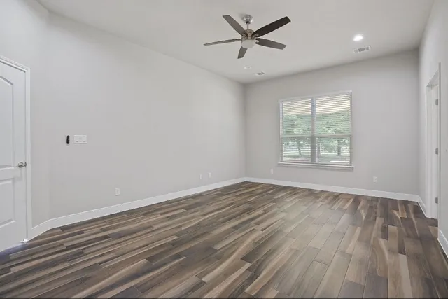 an empty room with wooden floor fan and windows