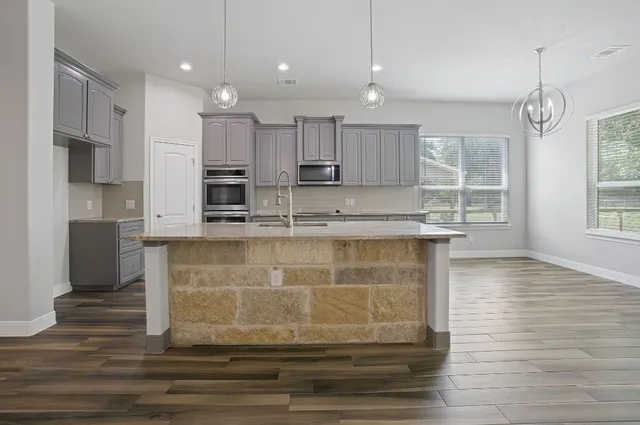 a kitchen with kitchen island granite countertop a stove a sink and white cabinets with wooden floor