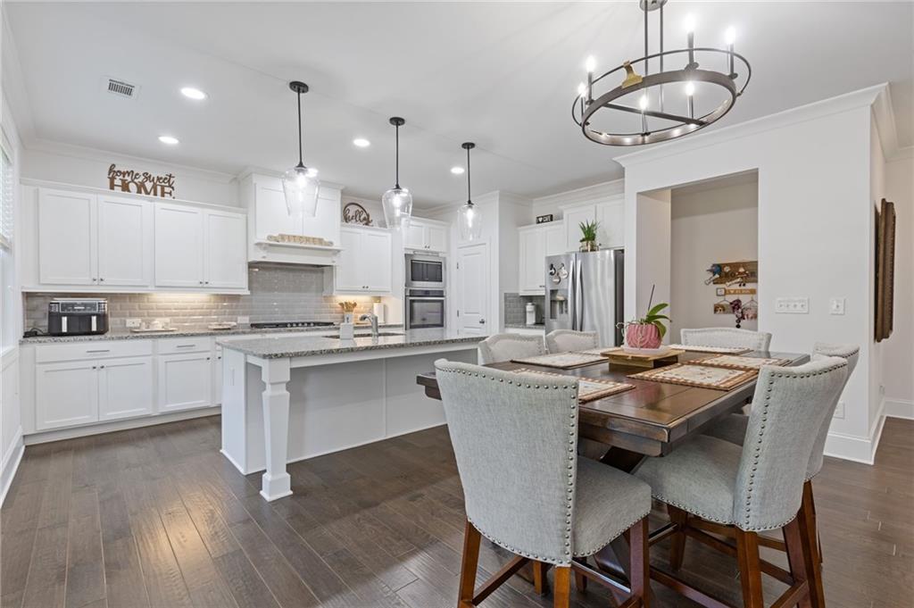 4867 Hunters Grove Way Sugar Hill, GA 30518 - Photo 16 of 61 a kitchen with stainless steel appliances kitchen island granite countertop a table chairs and white cabinets