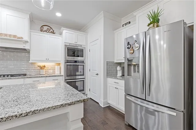 a kitchen with stainless steel appliances granite countertop a sink a stove a refrigerator and white cabinets