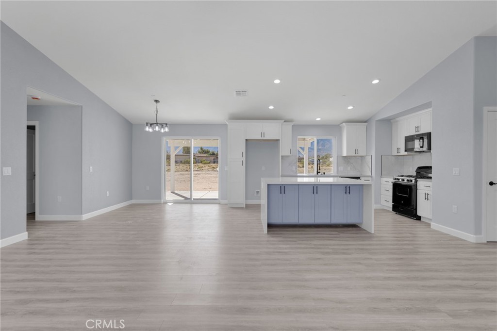 36165 Sutter Road Lucerne Valley, CA 92356 - Photo 13 of 42 a large white kitchen with kitchen island a sink wooden floor and a refrigerator