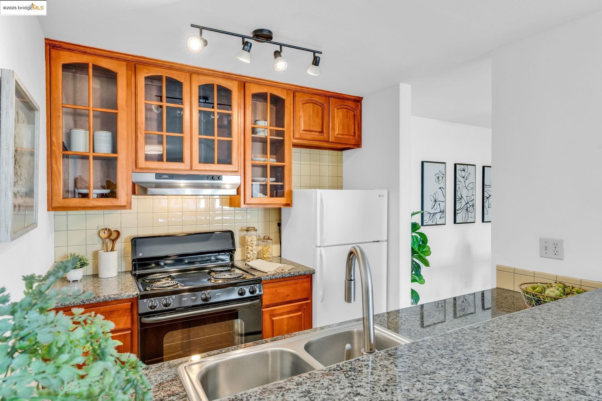 288 Whitmore Street, Unit 220 Oakland, CA 94611 - Photo 19 of 38 Kitchen featuring decorative backsplash, black electric range, freestanding refrigerator, brown cabinets, and under cabinet range hood