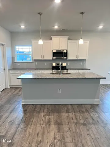 a kitchen with kitchen island granite countertop a sink cabinets and wooden floor