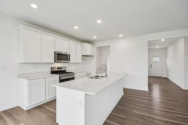 a kitchen with stainless steel appliances a stove top oven a sink a refrigerator white cabinets and wooden floor