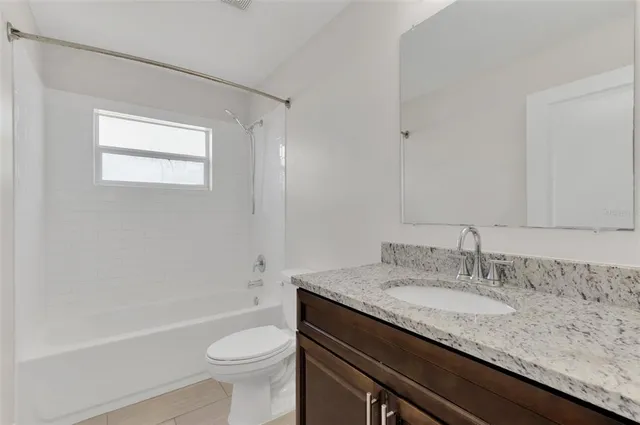 a bathroom with a granite countertop sink a toilet a mirror and bathtub