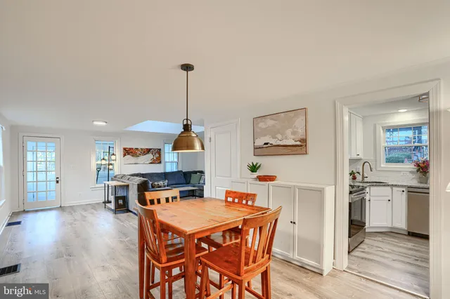 a open kitchen with stainless steel appliances granite countertop a stove top oven a sink a dining table and chairs with wooden floor