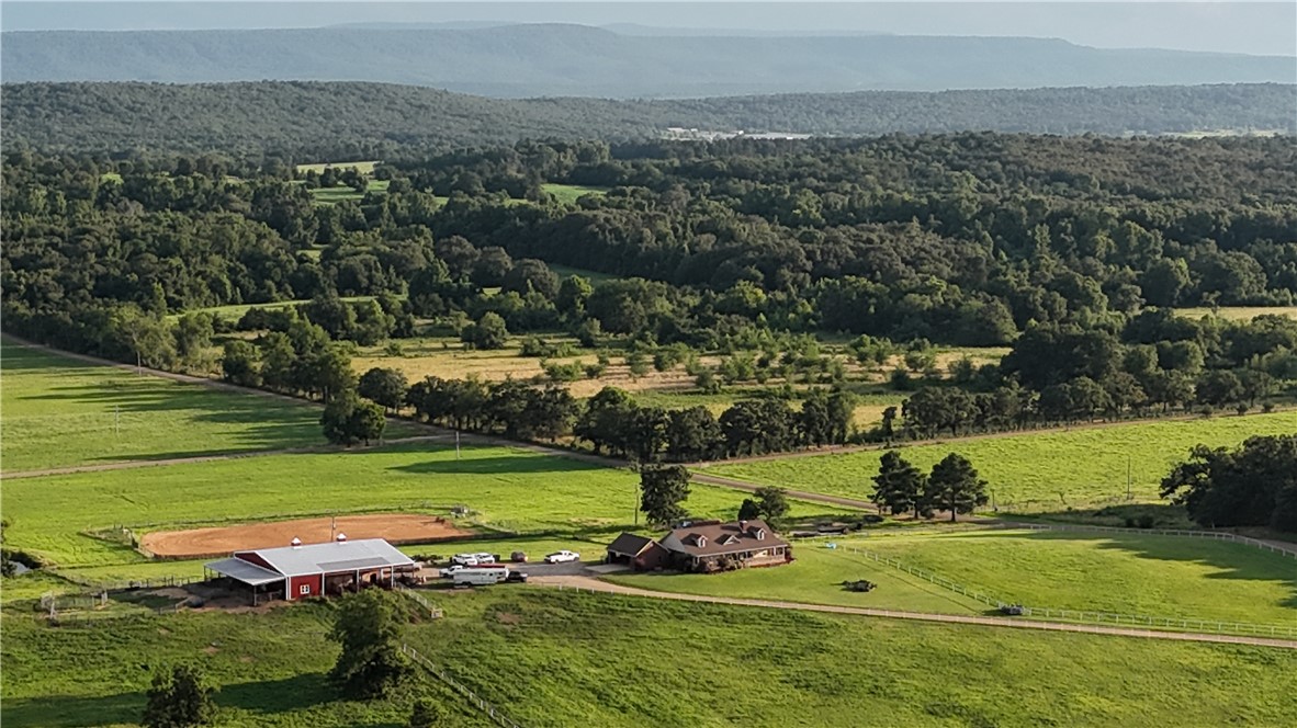 2210 Weiterer Road Scranton, AR 72863 - Photo 48 of 49 Expansive green pastures and wooded acreage featuring a red barn with a covered lean-to, an equestrian arena, and a stone-clad residence with a multi-gabled roofline