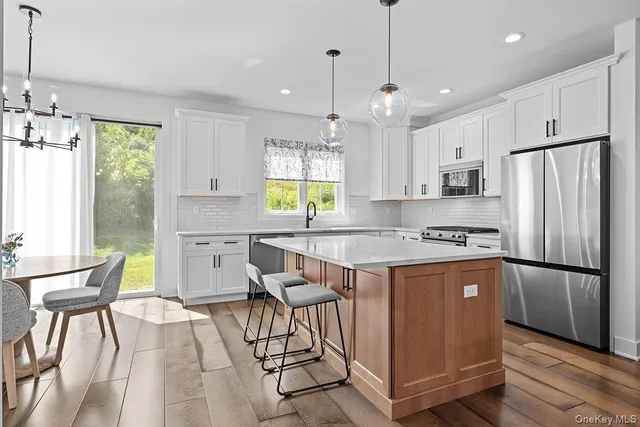 a kitchen with stainless steel appliances granite countertop a refrigerator a sink dishwasher a dining table and chairs with wooden floor