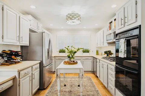 a kitchen with stainless steel appliances kitchen island granite countertop a refrigerator a stove a sink dishwasher and white cabinets with wooden floor