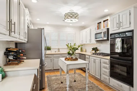 a kitchen with stainless steel appliances kitchen island granite countertop a refrigerator a stove a sink dishwasher and white cabinets with wooden floor
