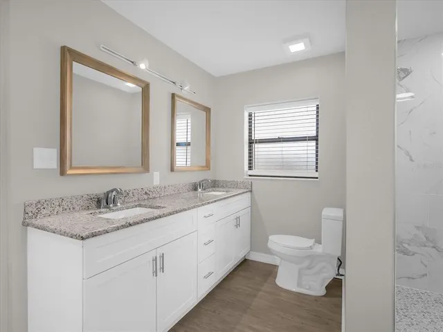 a bathroom with a granite countertop toilet a double vanity sink a mirror and a window