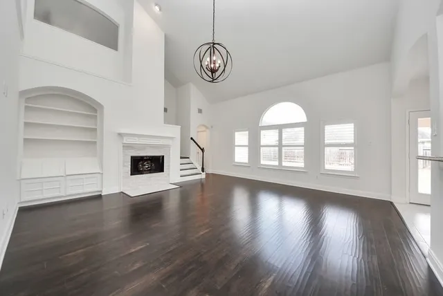 a view of an empty room with wooden floor fireplace and a window