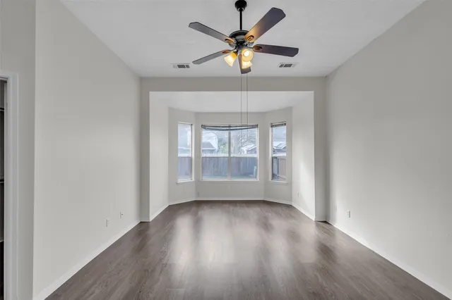 an empty room with wooden floor fan and windows