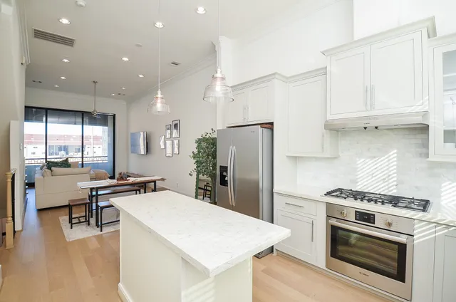 a kitchen with stainless steel appliances a stove a refrigerator and a dining table with wooden floor