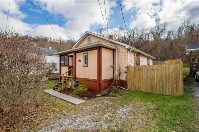 a view of a small house with yard and wooden fence