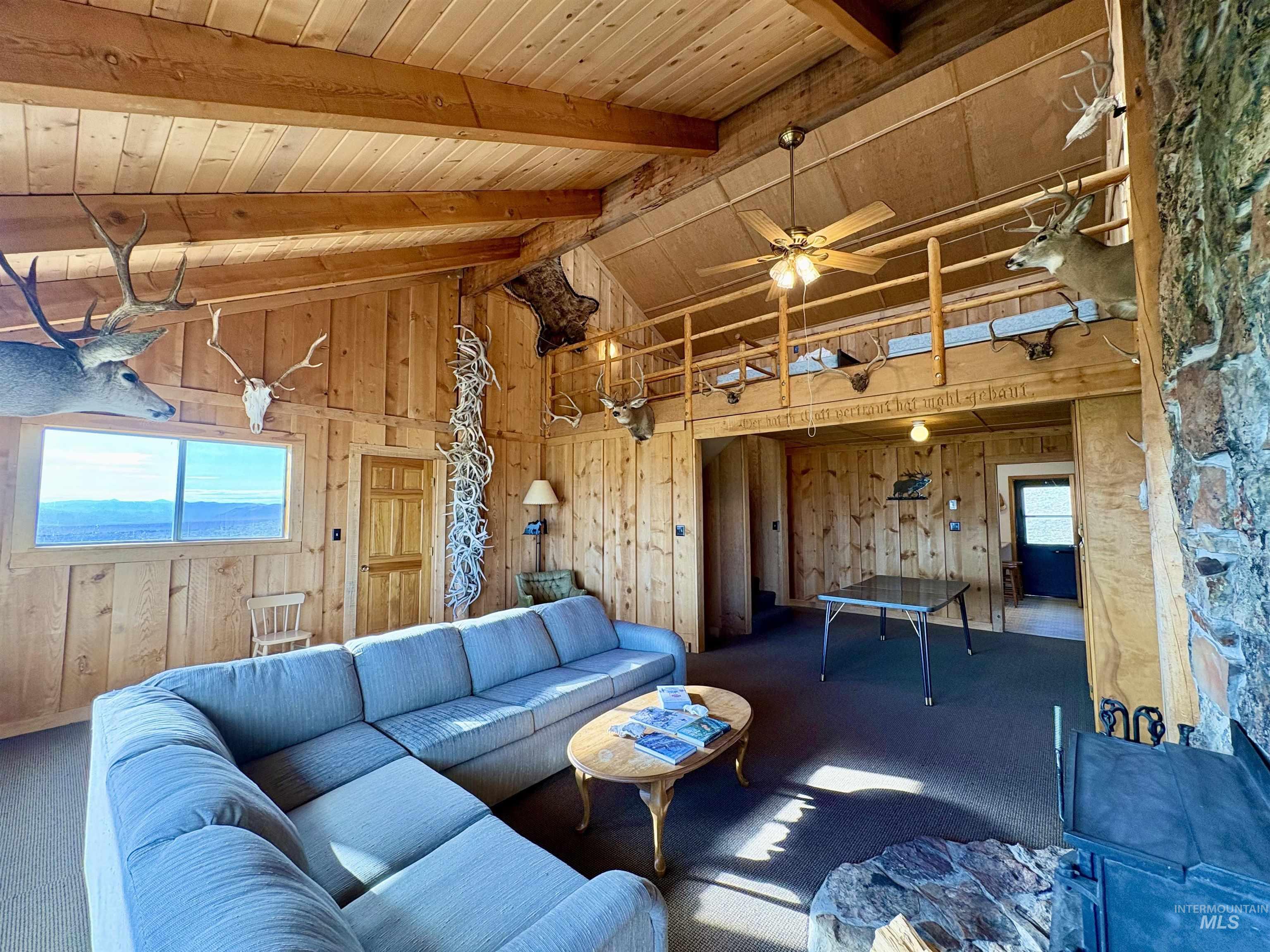 2040 Pahsimeroi River Road May, ID 83253 - Photo 3 of 29 Vaulted wood-paneled ceilings with exposed beams, an upper-level balcony, and a stone-clad hearth with a wood-burning stove