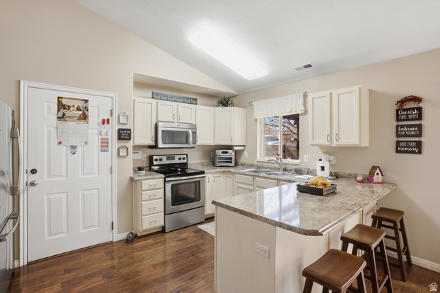 7737 Ranches Parkway Eagle Mountain, UT 84005 - Photo 7 of 28 Kitchen featuring vaulted ceilings, wood-finish flooring, white cabinetry, stainless steel appliances, and a peninsula countertop with seating