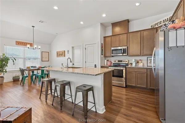 a kitchen with stainless steel appliances granite countertop a refrigerator a stove top oven a sink dishwasher a dining table and chairs with wooden floor