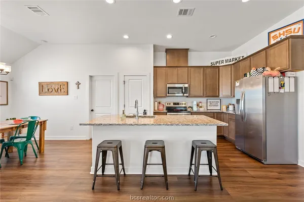 a kitchen with stainless steel appliances granite countertop a table chairs refrigerator and wooden cabinets