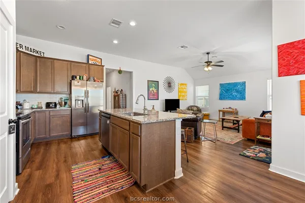 a large kitchen with stainless steel appliances refrigerator a stove top oven a sink dishwasher and wooden cabinets with wooden floor