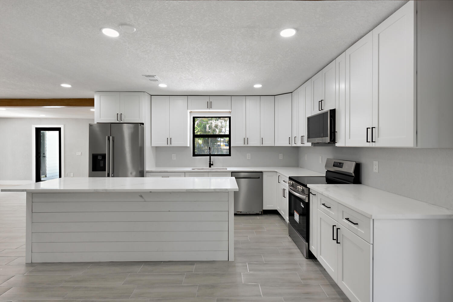 8587 Southwest 18th Avenue Stuart, FL 34997 - Photo 10 of 39 a large white kitchen with stainless steel appliances granite countertop a stove a sink dishwasher and a refrigerator with wooden floor
