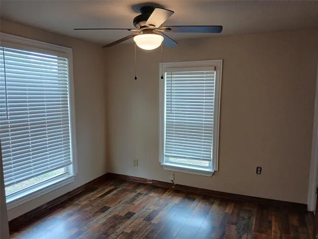 an empty room with wooden floor chandelier fan and windows