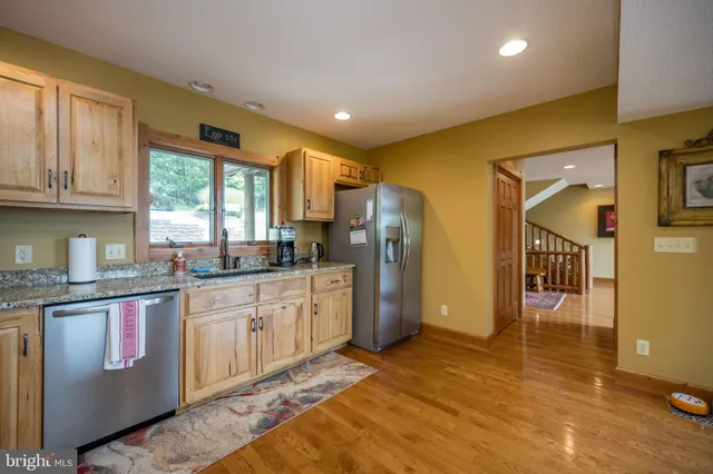 a kitchen with stainless steel appliances granite countertop a refrigerator a sink dishwasher a stove a dining table and chairs with wooden floor