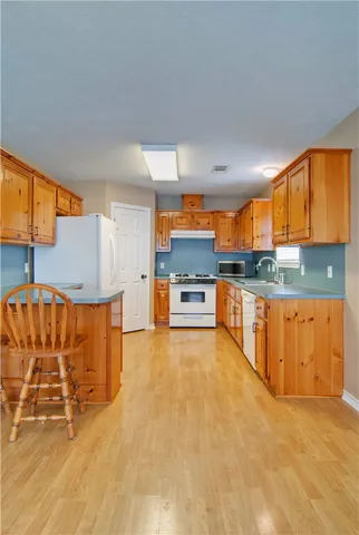 a view of a kitchen with kitchen island a sink stainless steel appliances wooden floor and a window