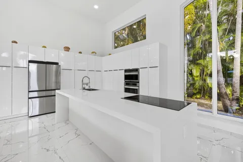 a large white kitchen with large window and stainless steel appliances