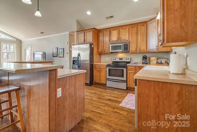 a kitchen with stainless steel appliances granite countertop a stove top oven a refrigerator a sink and dishwasher with wooden floor