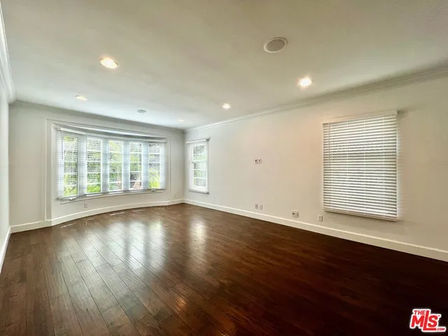 a view of an empty room with wooden floor kitchen view and a window