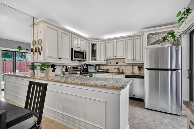 a kitchen with stainless steel appliances granite countertop a refrigerator a stove a sink dishwasher and white cabinets with wooden floor