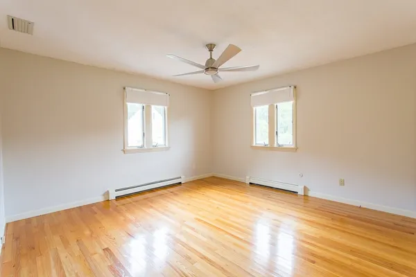 an empty room with wooden floor ceiling fan and windows
