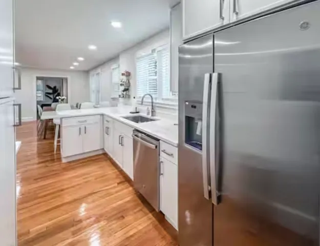 a large kitchen with a refrigerator a sink dishwasher a stove and white cabinets with wooden floor