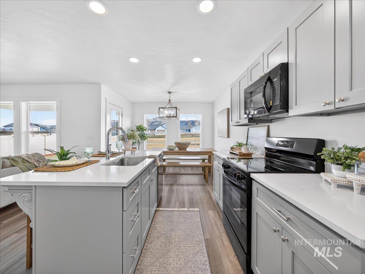 1410 Regency Way Emmett, ID 83617 - Photo 14 of 46 Kitchen with gray cabinets, black appliances, dark wood-style flooring, light stone counters, and a kitchen island with sink