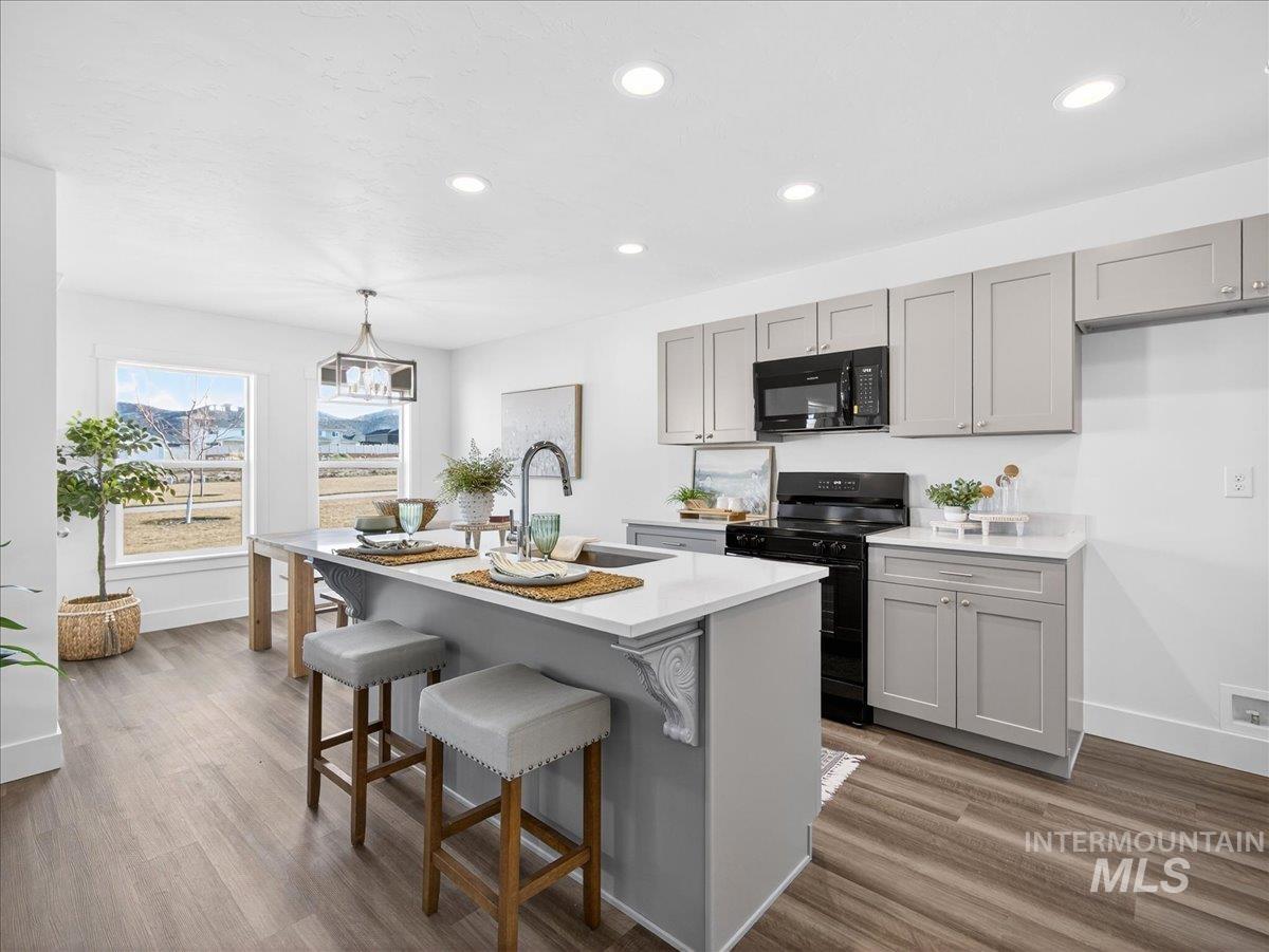 1410 Regency Way Emmett, ID 83617 - Photo 9 of 46 Kitchen with gray cabinets, black appliances, pendant lighting, a breakfast bar area, and dark wood-style floors