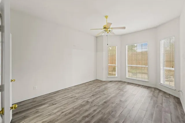 an empty room with wooden floor fan and windows