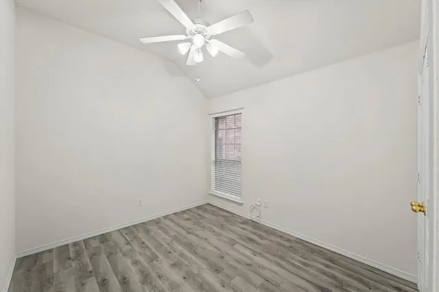 an empty room with a chandelier fan and wooden floor
