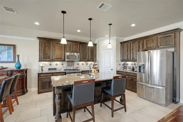 a kitchen with stainless steel appliances granite countertop a refrigerator a stove a sink a dining table and chairs