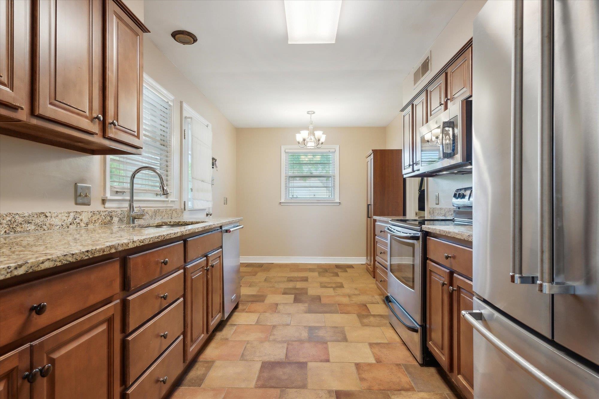 Kitchen with stainless steel appliances, an inviting chandelier, sink, light stone countertops, and light tile patterned flooring