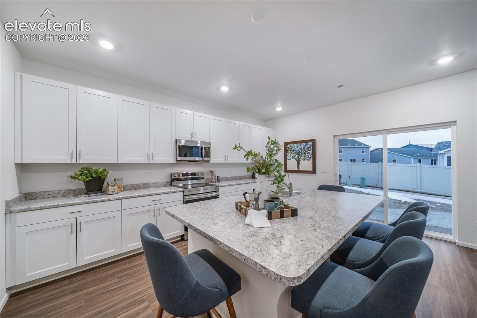 4936 Truscott Road Colorado Springs, CO 80925 - Photo 23 of 41 Kitchen featuring white cabinetry, stainless steel appliances, speckled stone countertops, a large island, and wood-finish flooring
*photos of a model home*